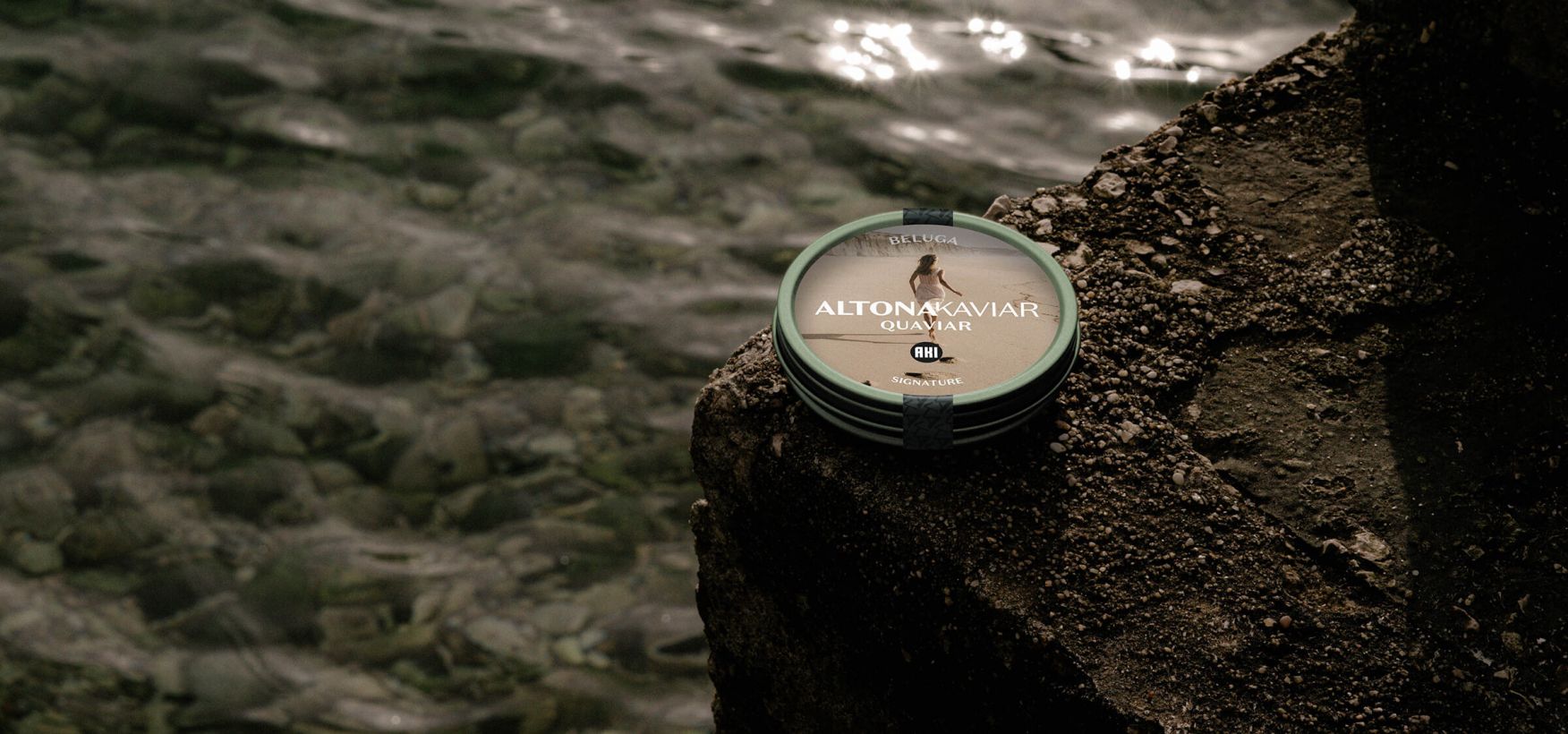 Eine grüne Kaviar Dose liegt auf einem steinigen Untergrund am Wasser.