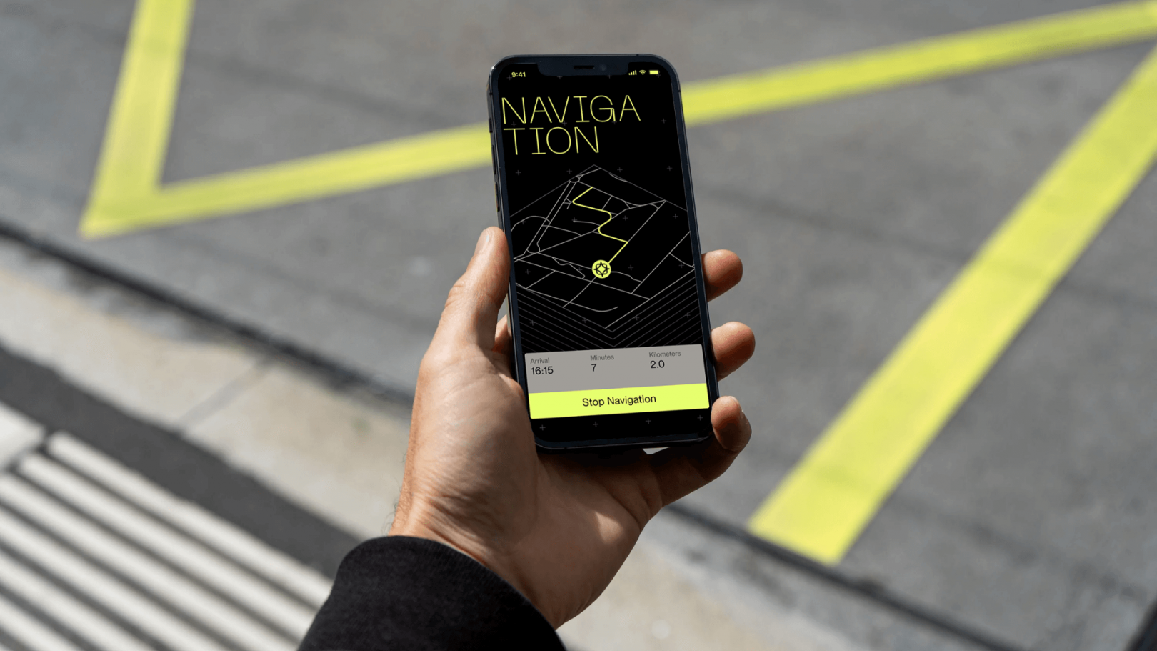 A hand holding a mobile phone on which the app is open. It shows a navigation. Asphalt background